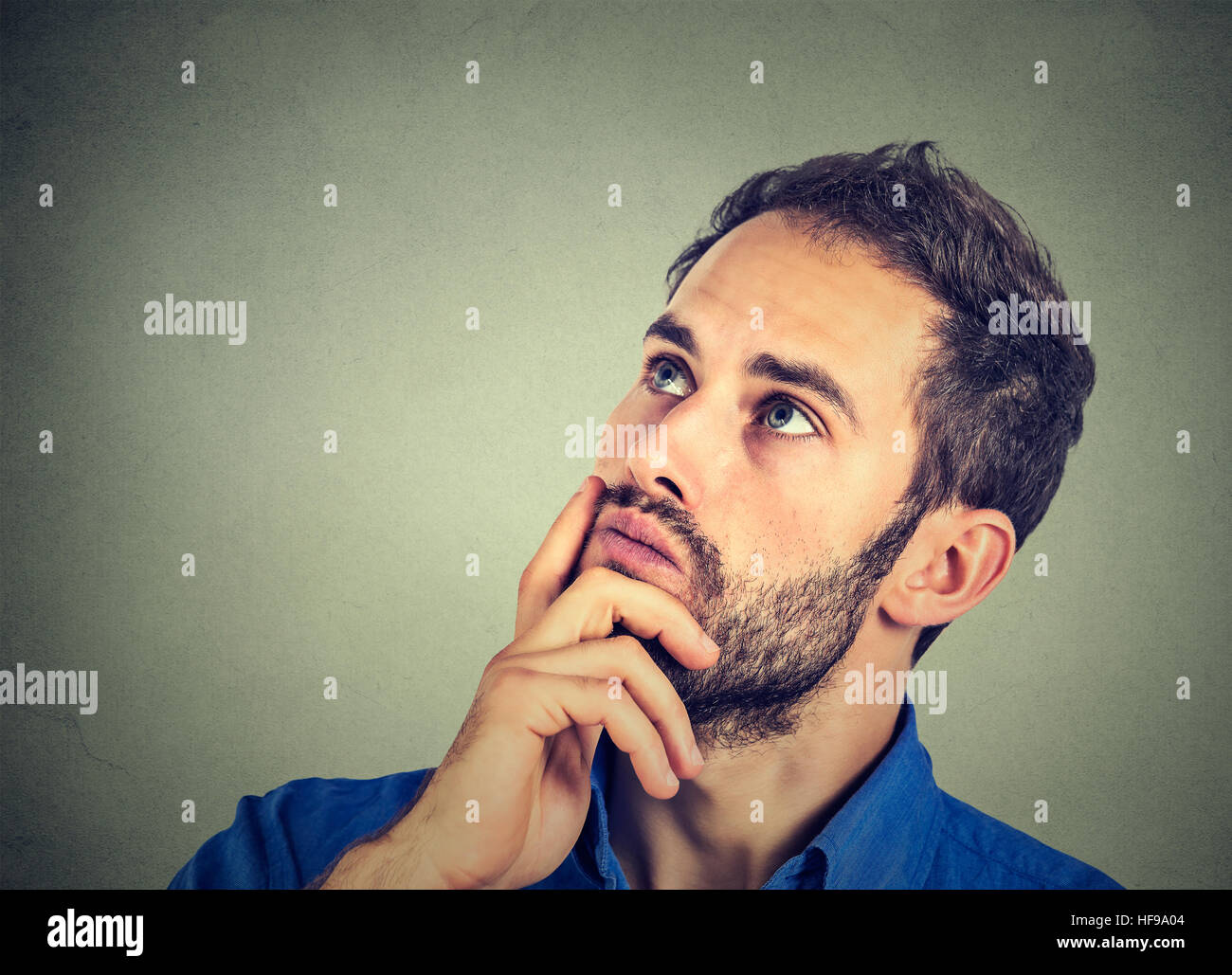Closeup ritratto di un uomo in appoggio il mento sulla mano pensando fantasticando, fissando attentamente verso l'alto, copia spazio a sinistra, isolato sul muro grigio backgroun Foto Stock