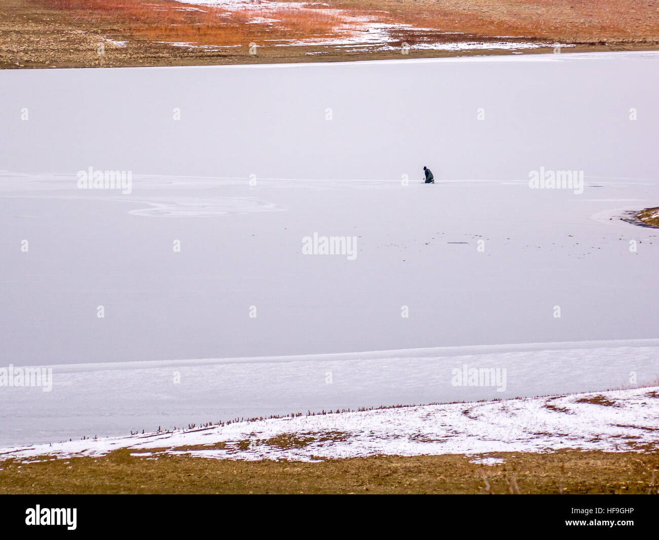 Pescatore di ghiaccio da solo sul lago ghiacciato di trinciatura di un foro! Foto Stock