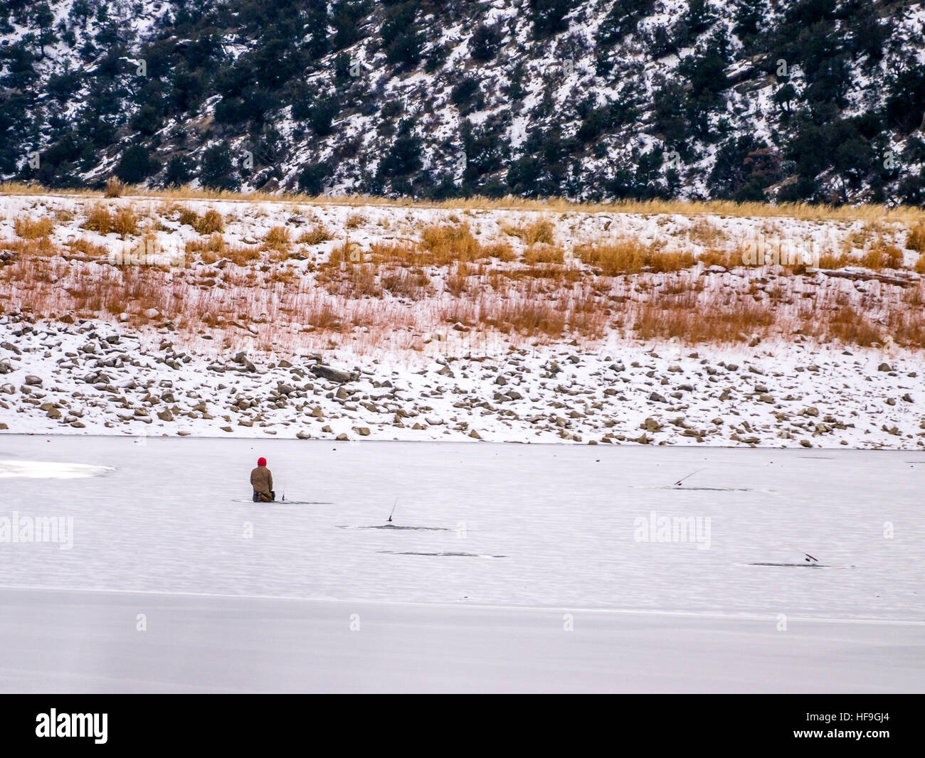 Solitario pescatore di ghiaccio inginocchiato in corrispondenza di un foro nel ghiaccio con la canna da pesca Foto Stock