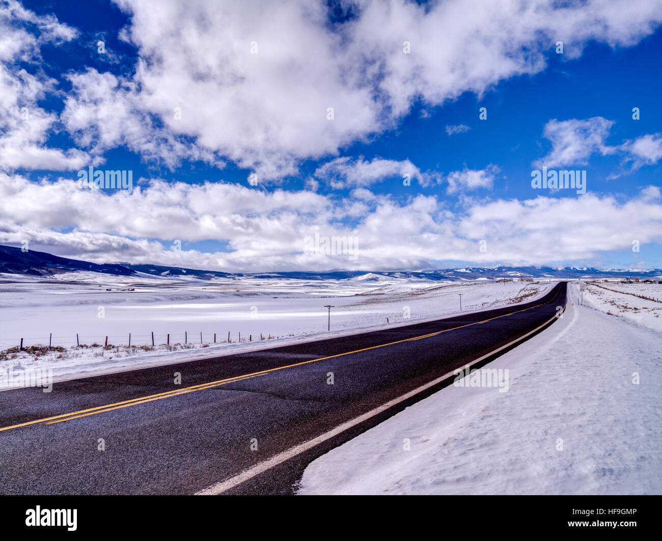 Carreggiata asfaltata si allunga in distanza, montagne e neve Foto Stock