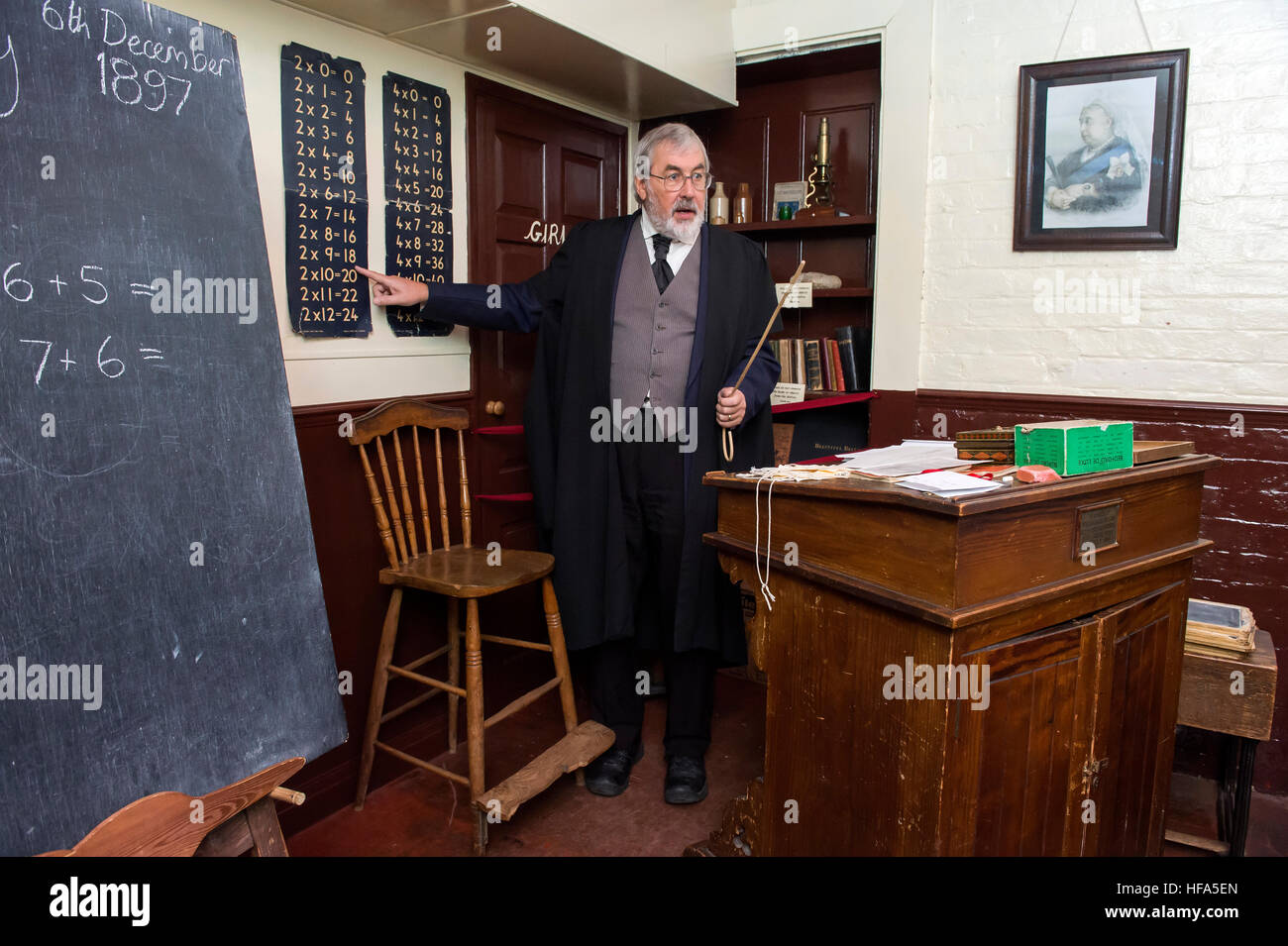 Una ricreazione di una classe in stile vittoriano. Un docente in possesso di una canna da zucchero l insegnamento della matematica e moltiplicazione su una lavagna. Foto Stock