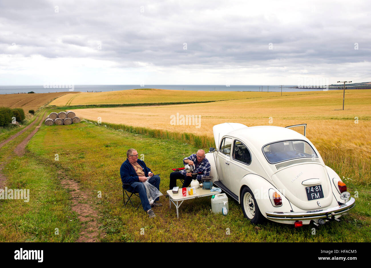 Due turisti olandesi hanno un picnic accanto alla loro VW Beetle in un campo vicino a St Abbs, Berwickshire, Scottish Borders, Scotland, Regno Unito Foto Stock