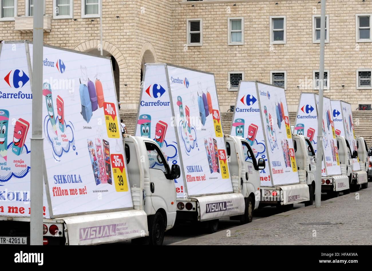 Cinque mobile advertising furgoni con manifesti di Carrefour nel centro di Tirana con lo slogan "hkolla fillon me ne', 'Scuola inizia con noi". Foto Stock