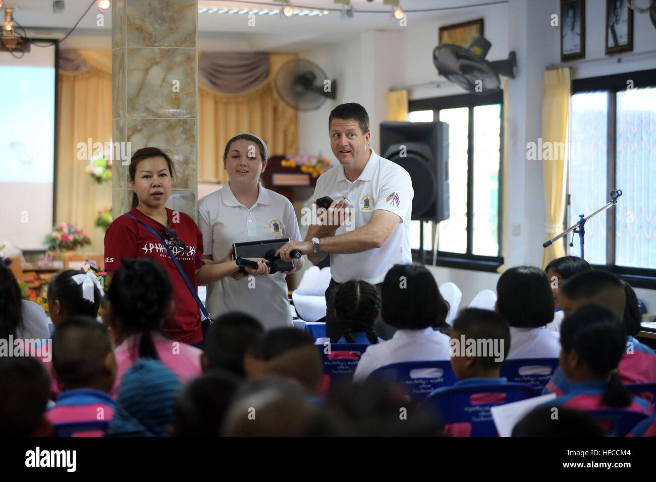 151221-N-IX266-009 CHANTHABURI, Thailandia (dec. n. 21) - Monnpapat Tudtanapun, un volontario per il Marriot Hotel di Pattaya, Rachel Kitzman, membro del Singapore Keystone Club, e il tenente La Cmdr. Glen D. Kitzman, cappellano militare comando Sealift Estremo oriente, riprodurre musica di vacanza per gli studenti di Pliu scuola elementare qui durante una recente comunicazione alla comunità evento. I volontari utilizzati musica innovative strategie e metodi creativi per insegnare inglese a più di 120 studenti. MSCFE e il Singapore Area Coordinator comunità a Singapore anche donato più di 1.200 libri in inglese per il Pong Nam R Foto Stock