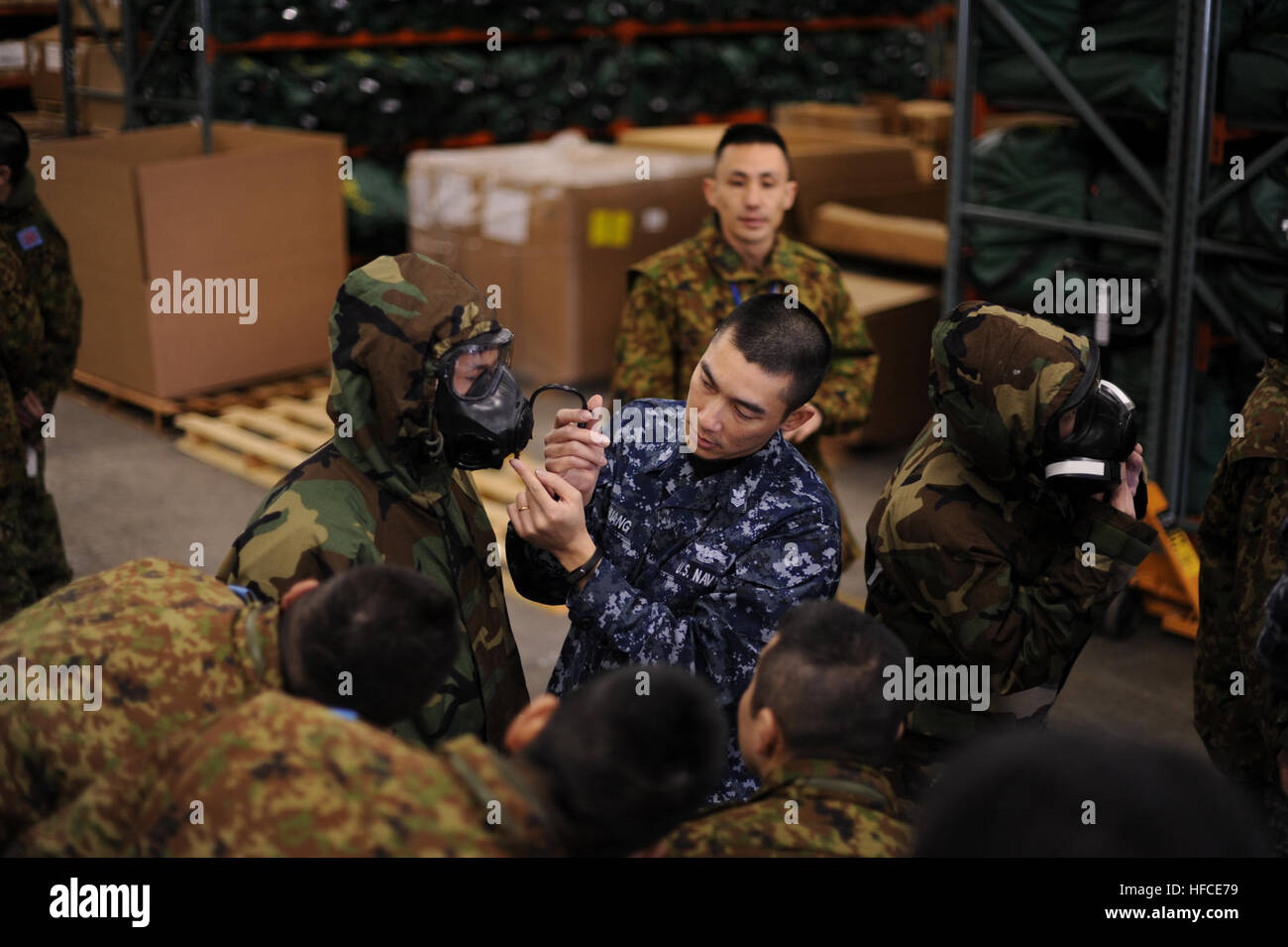 150226-N-CE644-301 Misawa combatté, Giappone (feb. 26, 2015) la manutenzione aeronautica Administrationman 1a classe Xiaojie Huang, assegnato alla Naval Air Facility (NAF) Misawa combatté di emergenza dell Ufficio di gestione, da Brooklyn, N.Y., centro incarica il Giappone terra Forza di Autodifesa (JGSDF) i soldati su come indossare correttamente chimico, biologico e protezione radiologica marcia a Misawa combatté la base dell'aria. La formazione ha dato i soldati JGSDF l opportunità di mettere in pratica la loro lingua inglese e capacità di ascolto durante la conduzione di tattiche militari negli Stati Uniti con gli elementi di servizio. (U.S. Navy foto di Senior Chief la comunicazione di massa spe Foto Stock