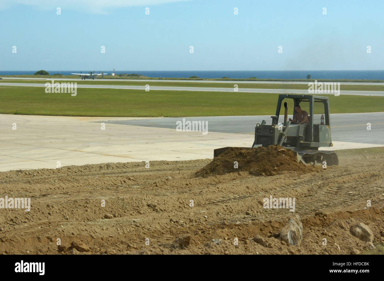 Navy Petty Officer 1. Classe Dennis Kowalczyk aziona una lama apripista a U.S. Stazione navale di Guantánamo Bay airfield, 20 gennaio, come un aereo atterra dietro di lui. La seabees stanno ampliando il campo di aviazione per i velivoli più grandi di terra a sostegno di funzionamento risposta unitaria, la fornitura di assistenza umanitaria ad Haiti. Stati Uniti Stazione navale Guatnanamo Bay Airfield 242519 di espansione Foto Stock