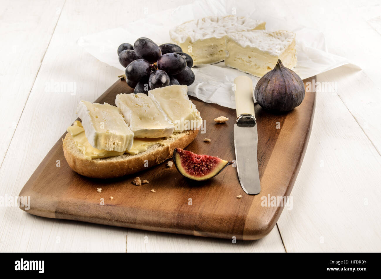 Metà panino con camembert su una tavola di legno, anche con una figura e uve rosse Foto Stock