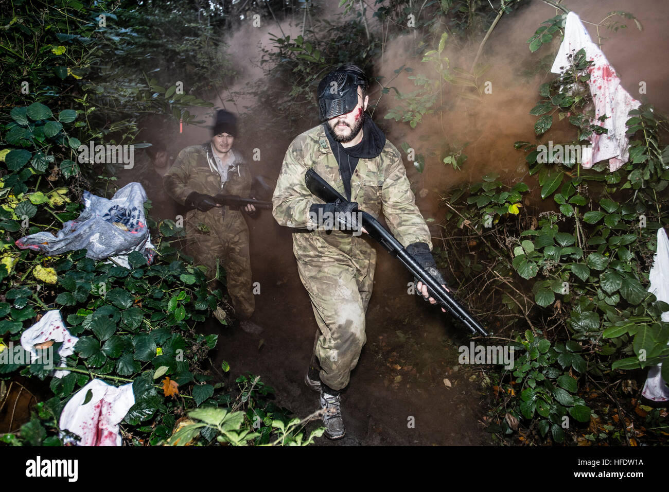 Gruppi di persone vestite in combattimento camouflage uniformi e trasportare vernice-ball pistole zombie di caccia nei boschi in un 'The Walking Dead esperienza' Azione Live gioco di ruolo (LARP) attività evento su un pomeriggio di novembre nei boschi vicino a Aberystwyth Wales UK Foto Stock