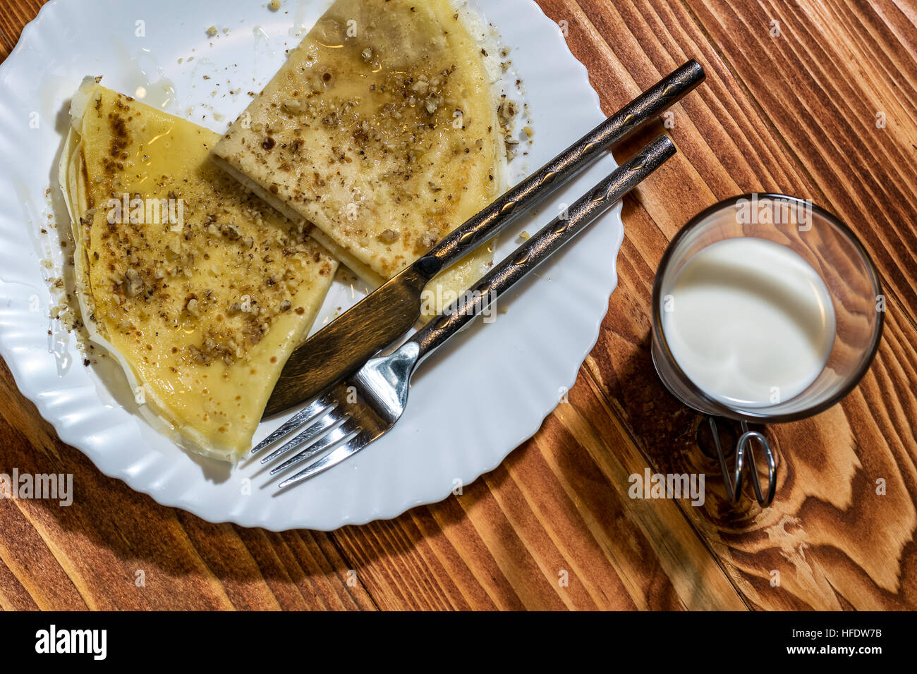 Crepes Pancake con miele e noci in una piastra ed un bicchiere di latte su un tavolo di legno Foto Stock
