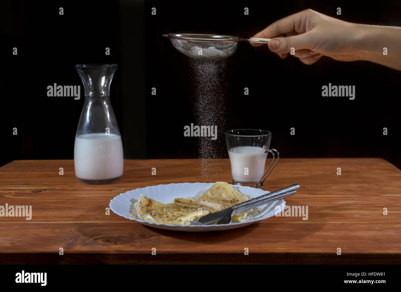 Crepes Pancake con miele e noci, latte in vetro e bottiglia e versa manualmente lo zucchero in polvere su di un tavolo di legno Foto Stock