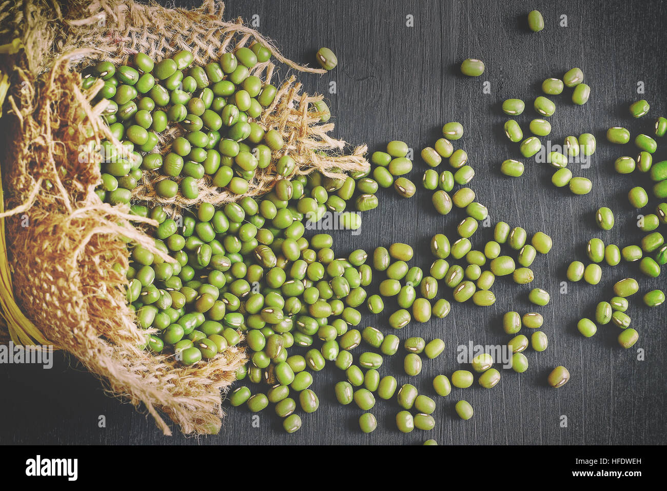 Fagioli (Vigna radiata) fuoriuscita dal sacchetto di tela nera su sfondo di legno. Vista superiore Foto Stock