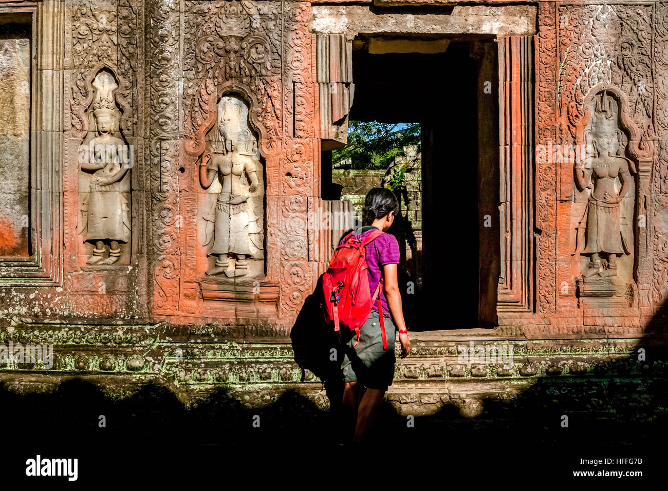 Una donna sta camminando davanti ad un muro decorato con bassorilievo di figure apsara, dove un ingresso si trova a Ta Prohm, Siem Reap, Cambogia. Foto Stock