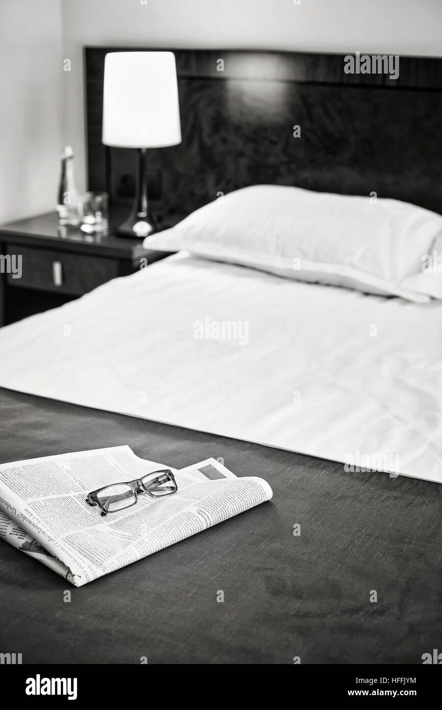 Foto in bianco e nero di un giornale e bicchieri su un letto d'albergo, il fuoco selettivo. Foto Stock