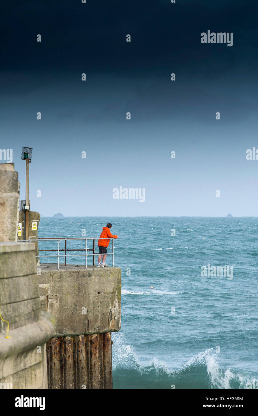 Un uomo in piedi sulla banchina del porto che si affaccia sull'ingresso a Newquay Harbour in Cornovaglia, Inghilterra, Regno Unito. Foto Stock