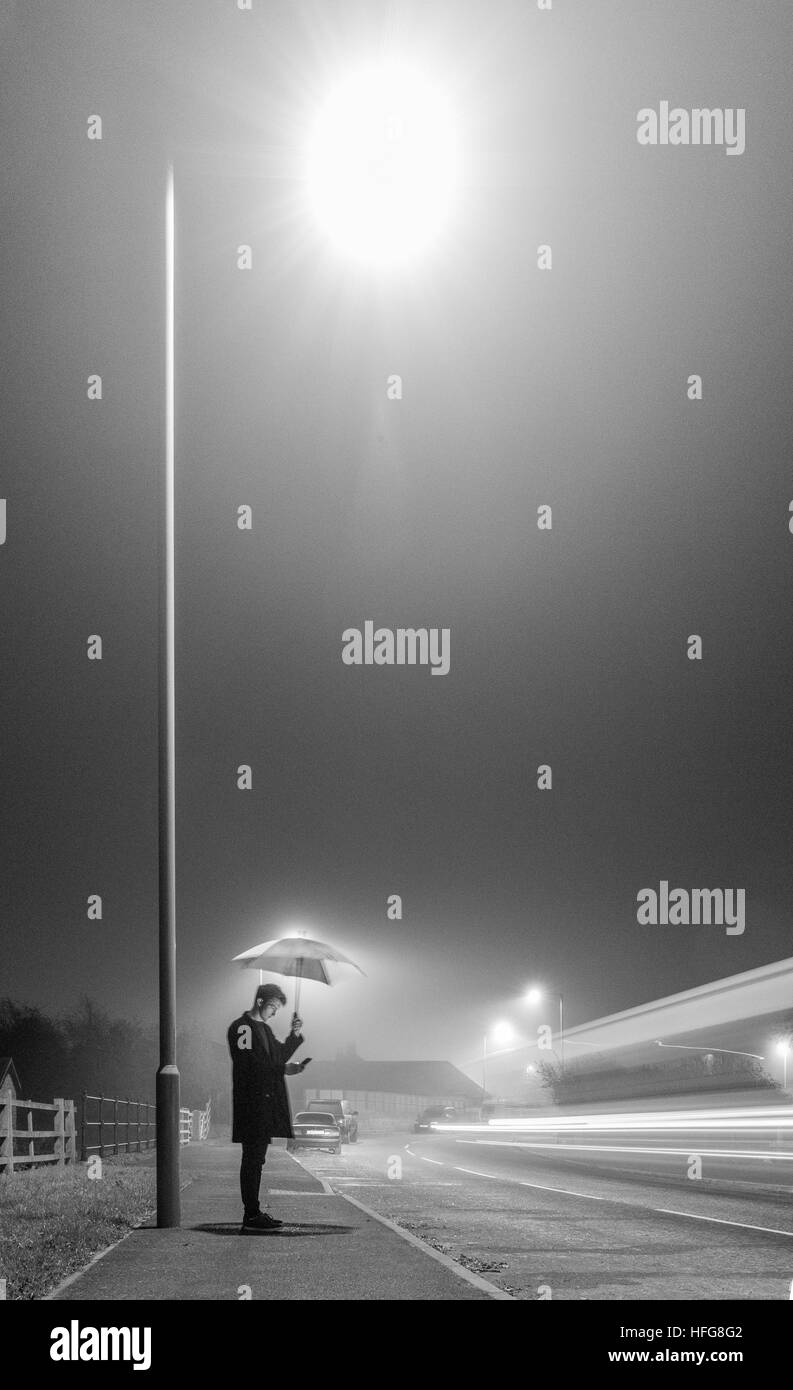 Giovane uomo sotto il lampione con ombrellone sulla serata di nebbia Foto Stock