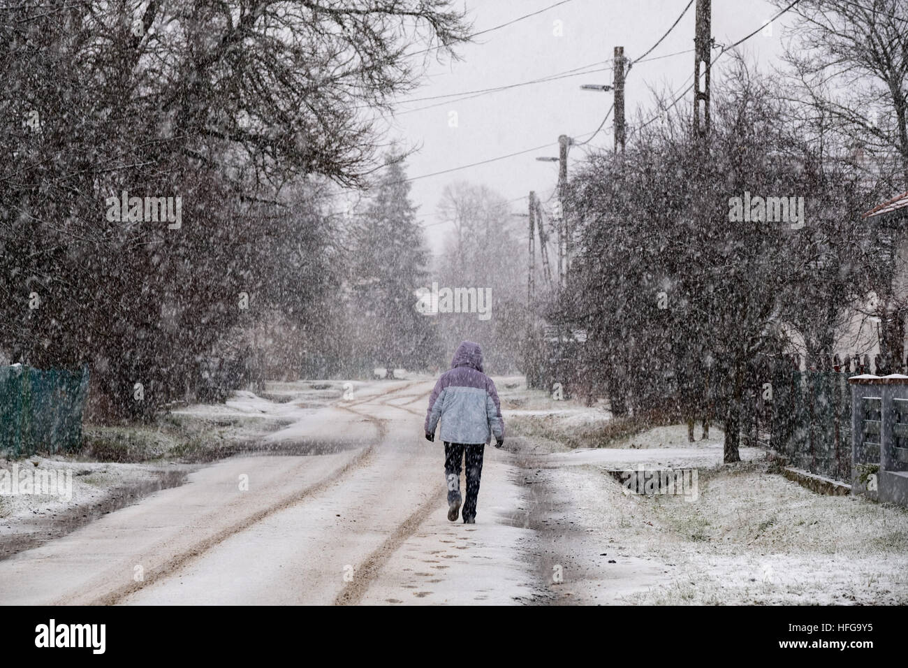 Una donna che cammina sulla strada principale di un villaggio durante la nevicata Foto Stock