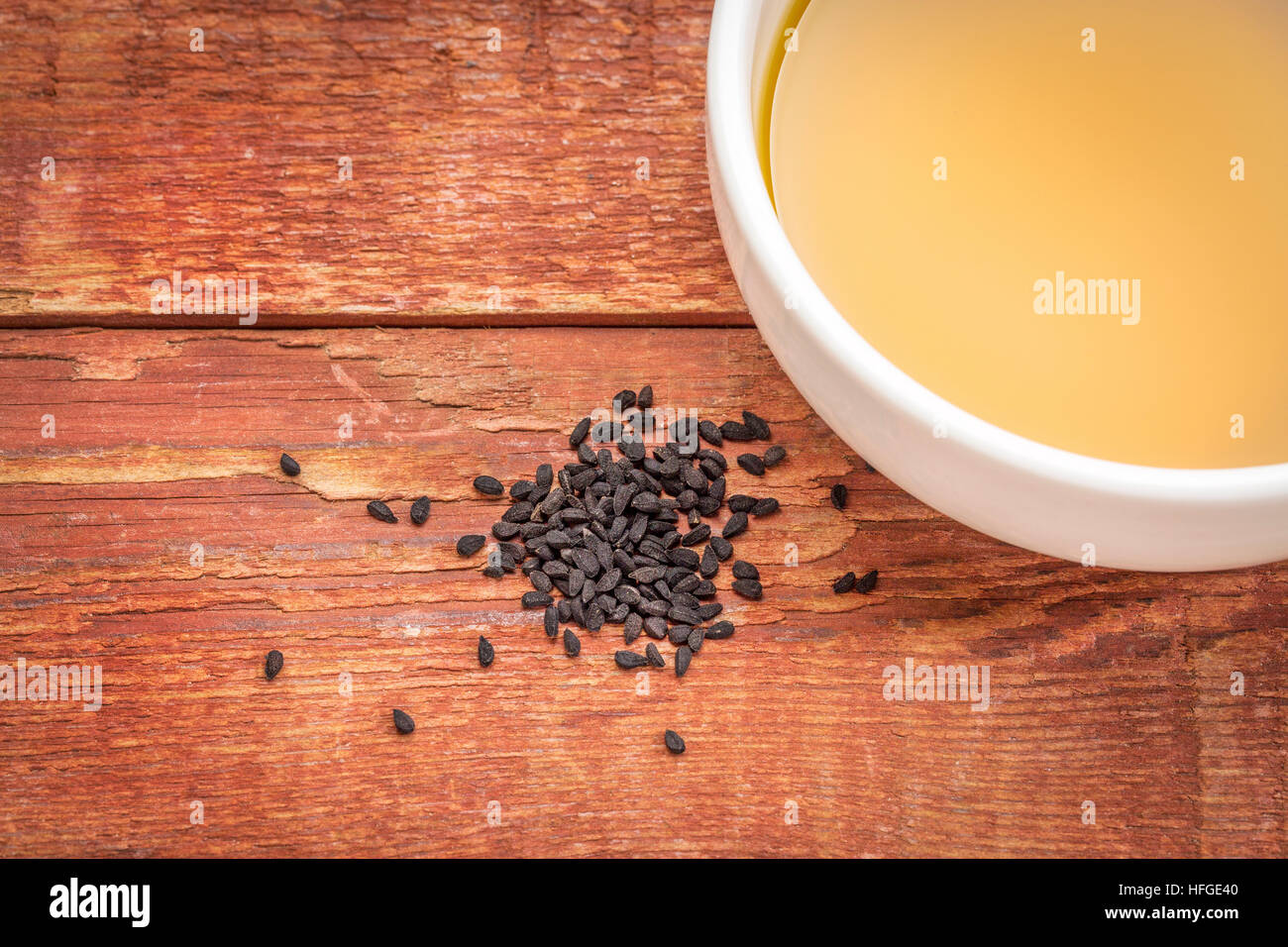 Nero semi di cumino (Nigella sativa) e l'olio in un recipiente piccolo contro rustico in legno di crusca Foto Stock