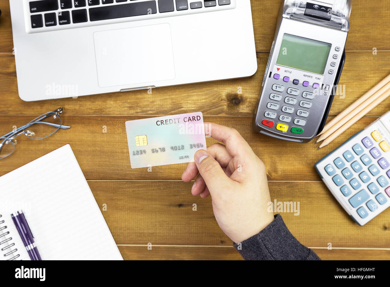 Mano del cassiere in possesso di una carta di credito su macchina EDC o terminale carte di credito con la calcolatrice e bicchieri. La carta di credito su banca giapponese note. Foto Stock