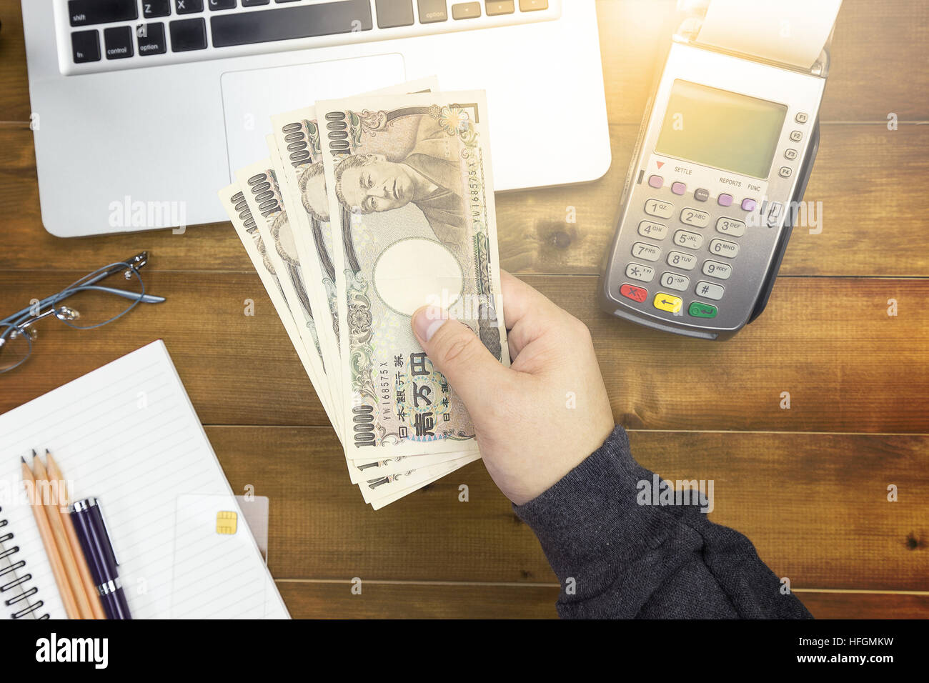 Un cassiere mano azienda valuta giapponese (yen) con oltre cassiere scrivania con lettore di carte di credito la penna e il computer portatile. Foto Stock