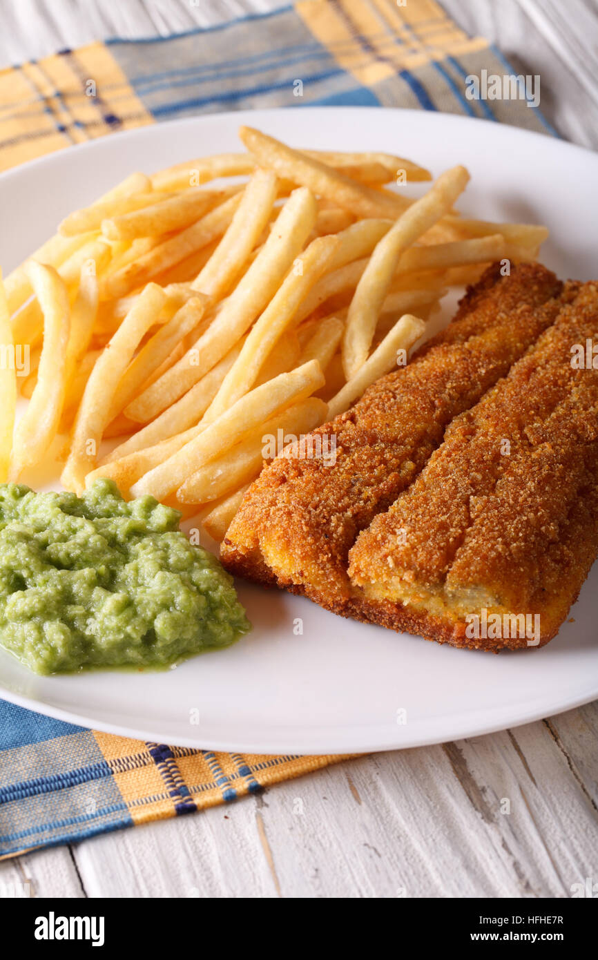 Cibo inglese: fritto di filetti di pesce e patatine e purea di piselli close-up su una piastra. In verticale Foto Stock