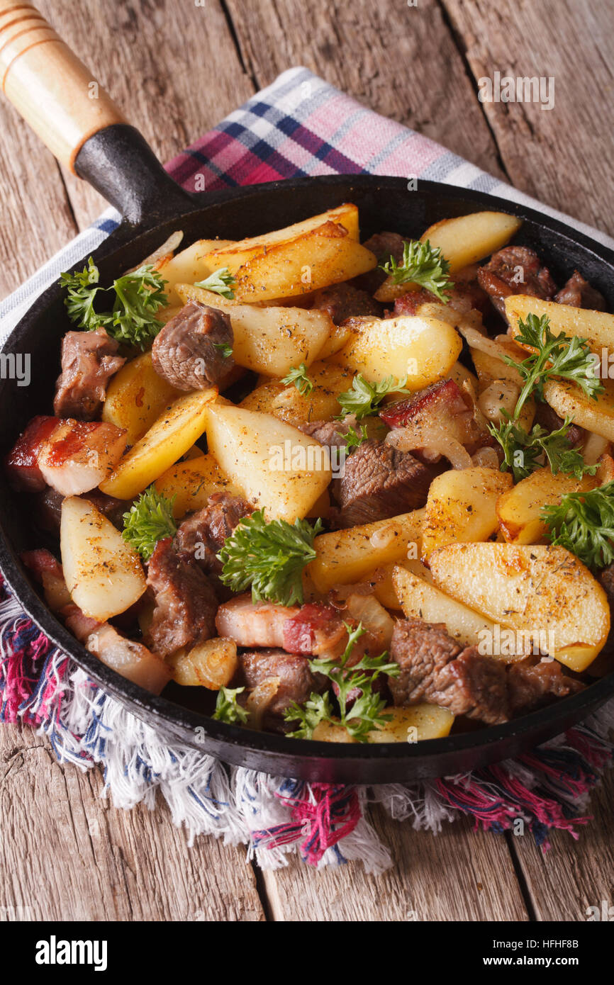 Paese caldo patate fritte con carne e la pancetta servita in una padella di close-up verticale. Foto Stock