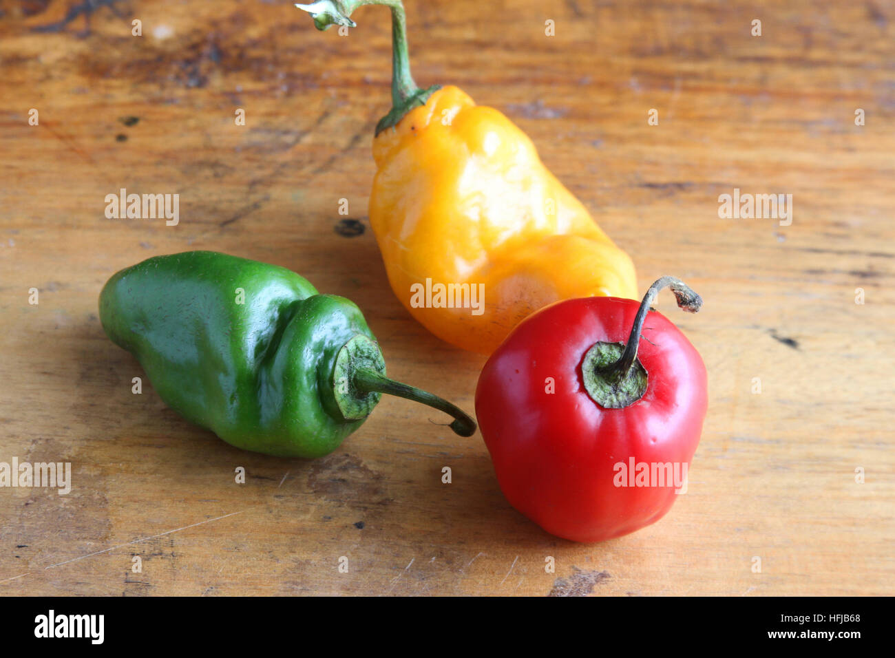 Tre coloratissimi peperoncini, uno rosso, uno verde e uno giallo, su un tavolo Foto Stock