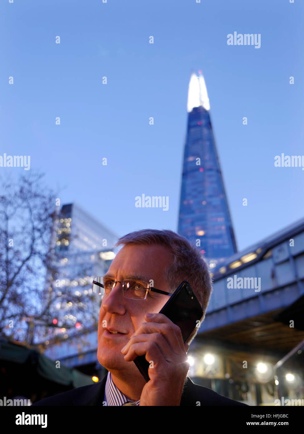 Città imprenditore all'aperto a parlare sul suo jet black iPhone 7 plus al crepuscolo con 'l'Shard' torre in background London SE1 Foto Stock