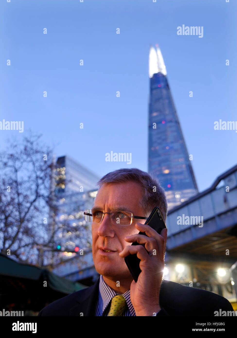 Città imprenditore all'aperto a parlare sul suo jet black smartphone iPhone 7 plus al crepuscolo con 'l'Shard' torre in background London SE1 Foto Stock