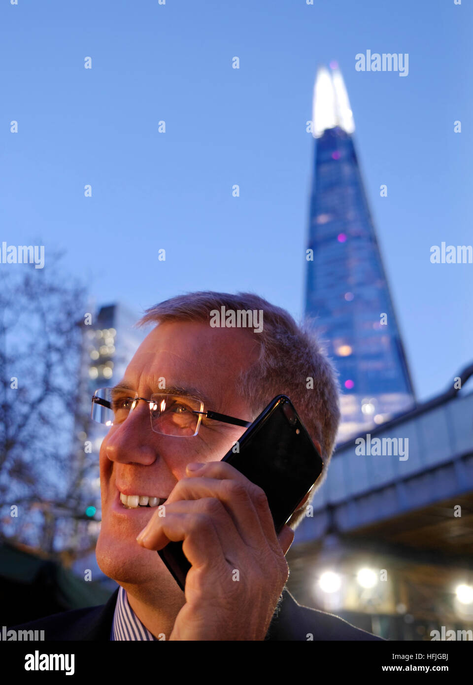 Città sorridente uomo uomo d affari esterni di parlare un buon business news sul suo iPhone 7 plus al crepuscolo con 'l'Shard' torre in background London SE1 REGNO UNITO Foto Stock