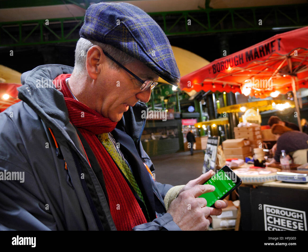 Uomo maturo con shopping bag, tenendo smartphone iPhone 7 plus, con detox 'pulito' dieta suggerimenti su schermo interattivo, Borough Market stall dietro di notte. London REGNO UNITO Foto Stock