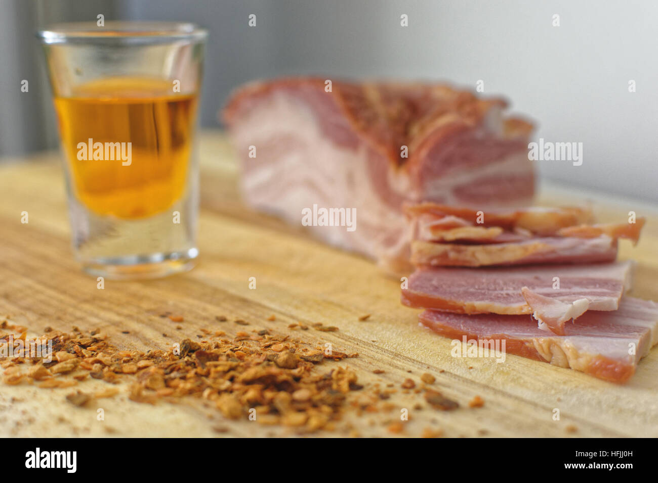 Bacon fresco su un piatto di legno con un bicchiere di brandy arancione Foto Stock