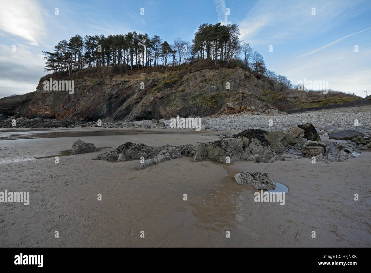 Dalla spiaggia guardando verso una scogliera rocciosa con matura abeti su top e rive digradanti su entrambi i lati con il blu del cielo. Foto Stock