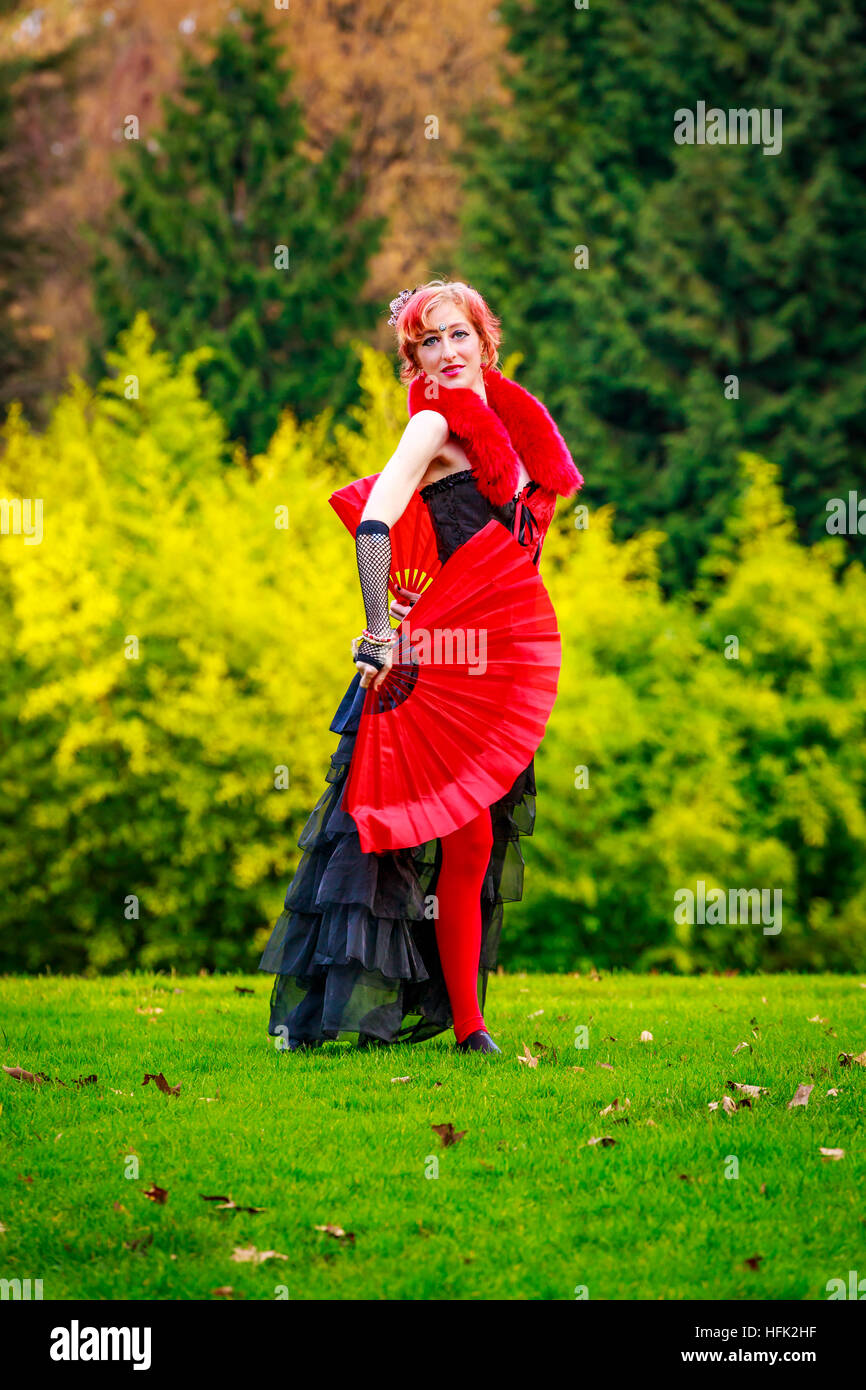 Giovane bella donna in costume di circo gioca con ventole di rosso nel parco. Foto Stock