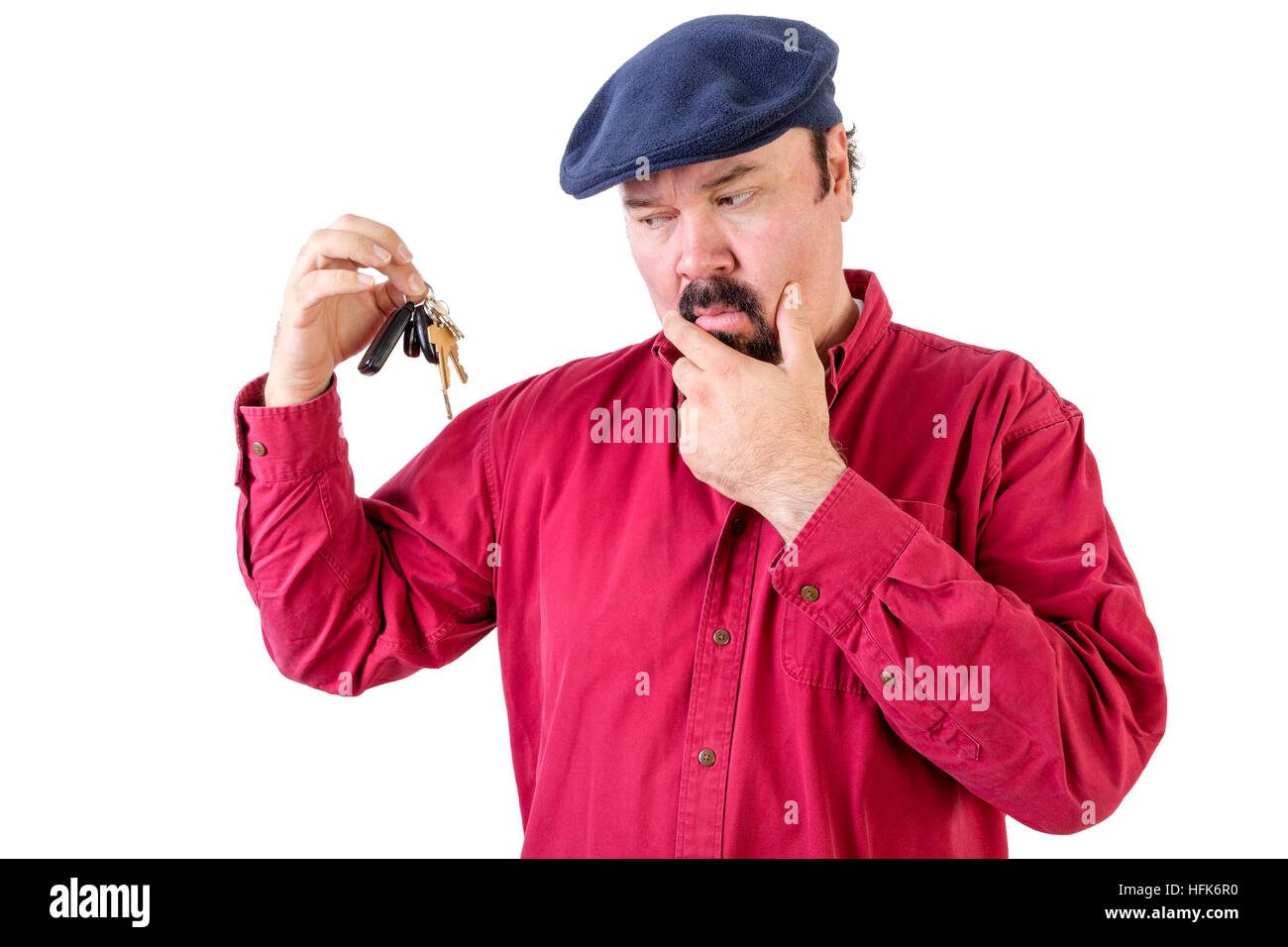 Confuso uomo accigliata in un mazzo di chiavi della macchina con un espressione pensosa come egli riflette su ciò che egli dovrebbe fare con loro ora che egli abbia raggiunto h Foto Stock