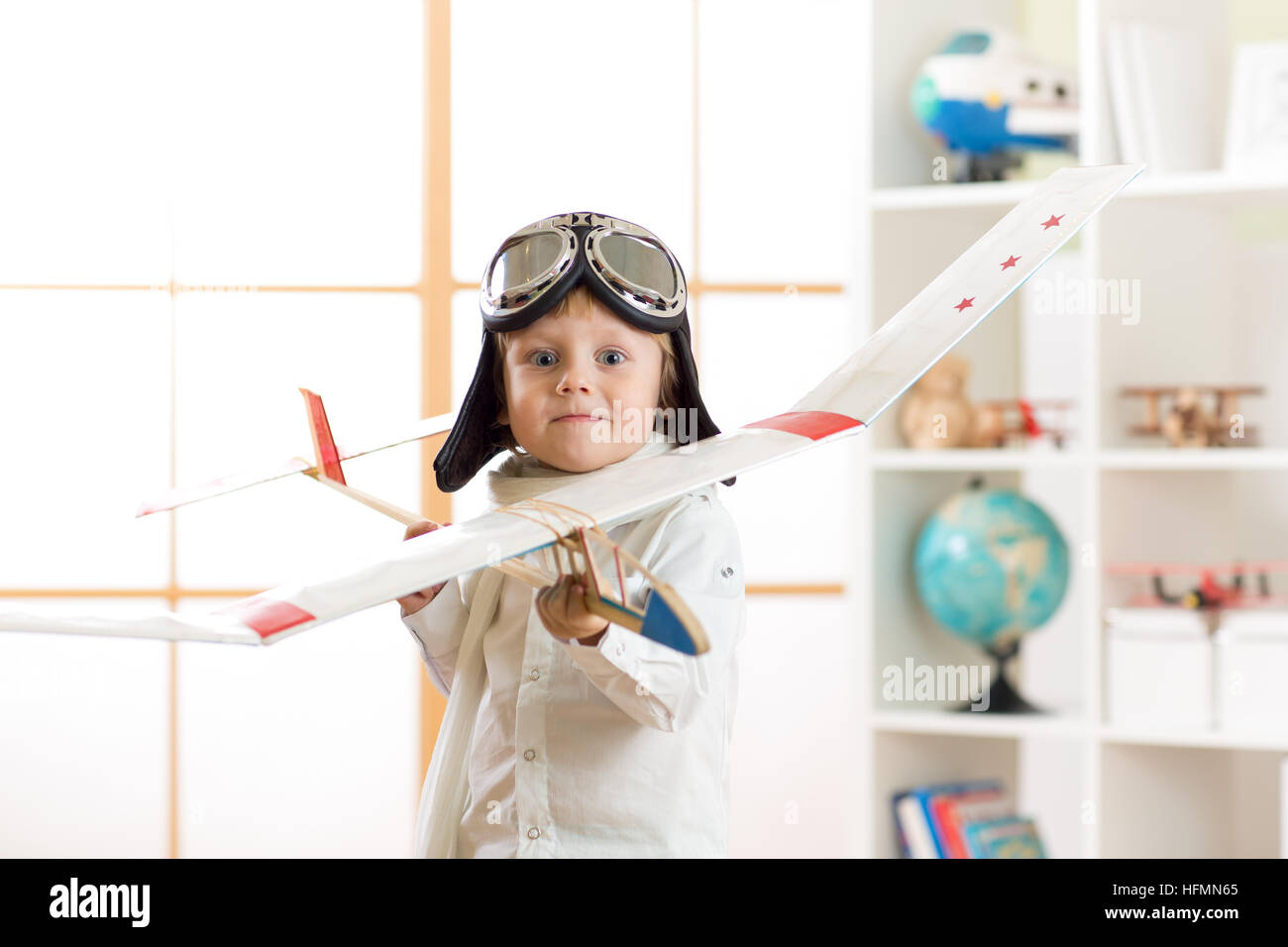 Ragazzo bambino vestito come un pilota con aeroplano giocattolo giocare in casa Foto Stock