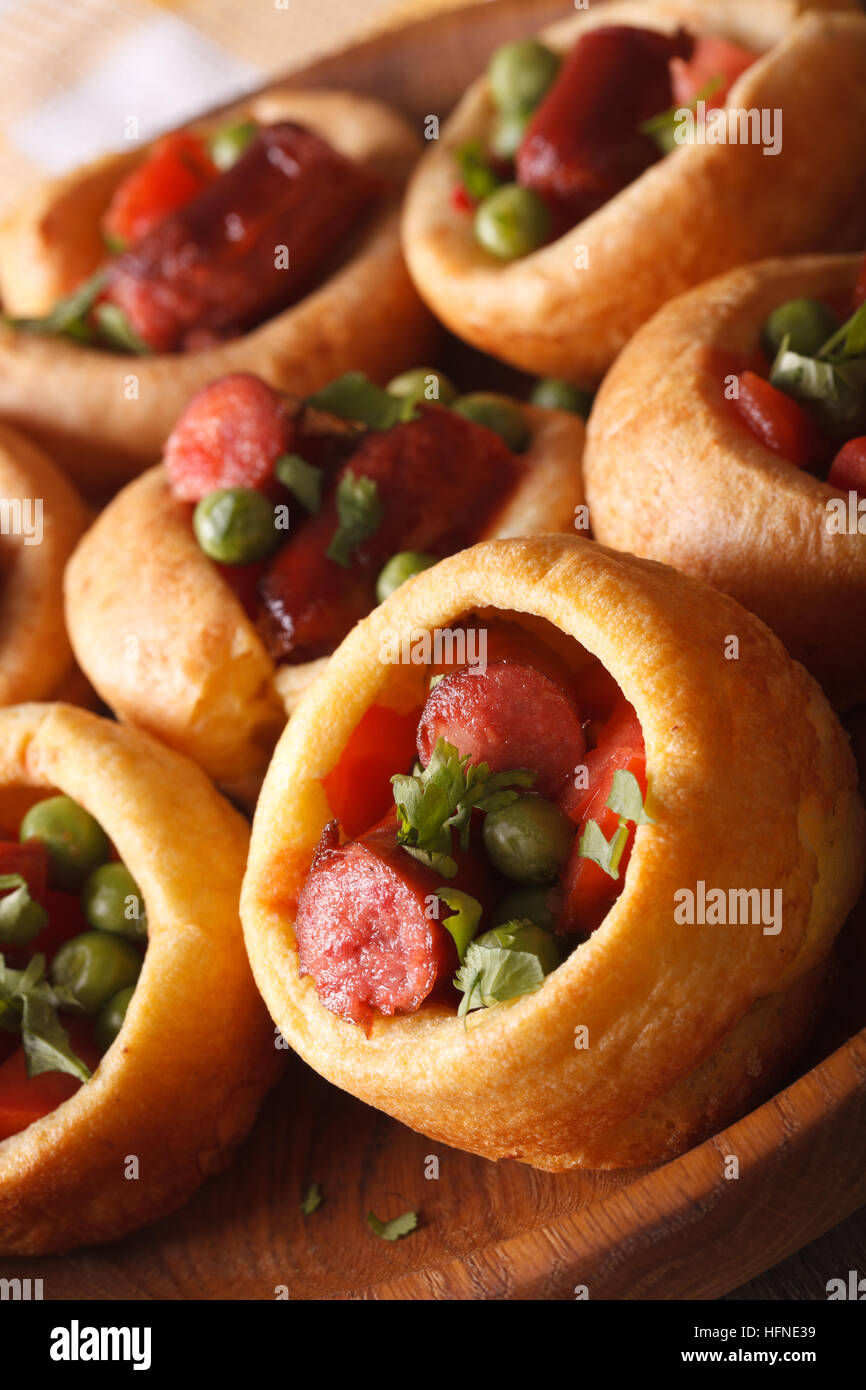 Yorkshire pudding con salsicce, erbe e piselli verdi close-up verticale. Foto Stock