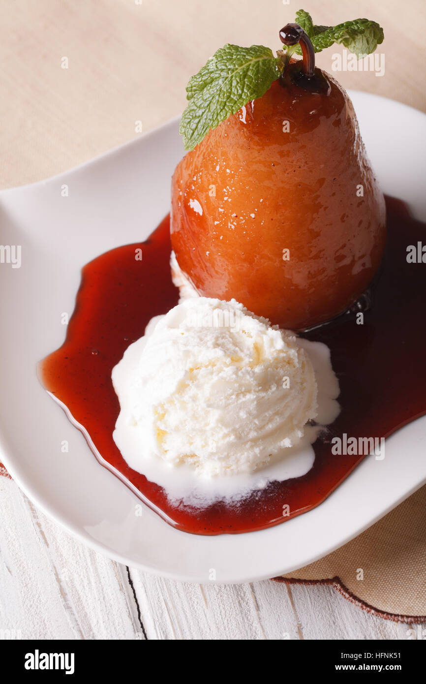 Dessert: pera affogata e gelato alla vaniglia close-up su una piastra verticale. Foto Stock