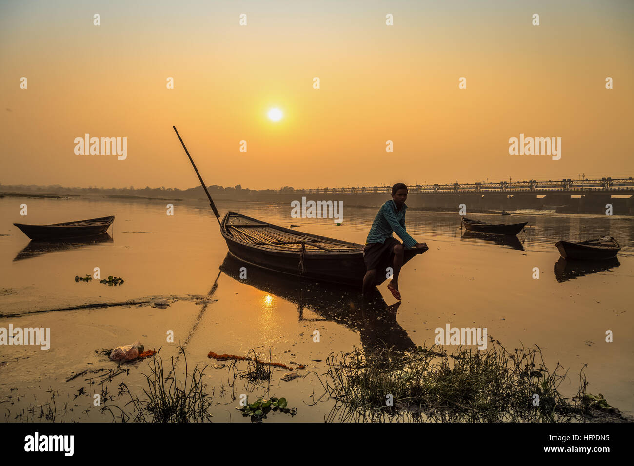 Un rematore siede sul suo ancorata la barca di legno al tramonto sul fiume Damodar vicino al Durgapur Barrage, West Bengal, India. Foto Stock