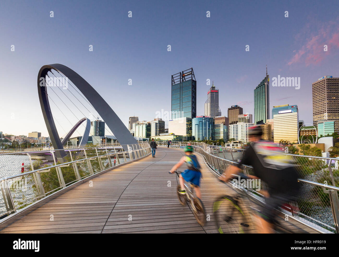 I ciclisti che attraversano la banchina di Elizabeth bridge al crepuscolo con lo skyline della città al di là, Perth, Australia occidentale, Australia Foto Stock