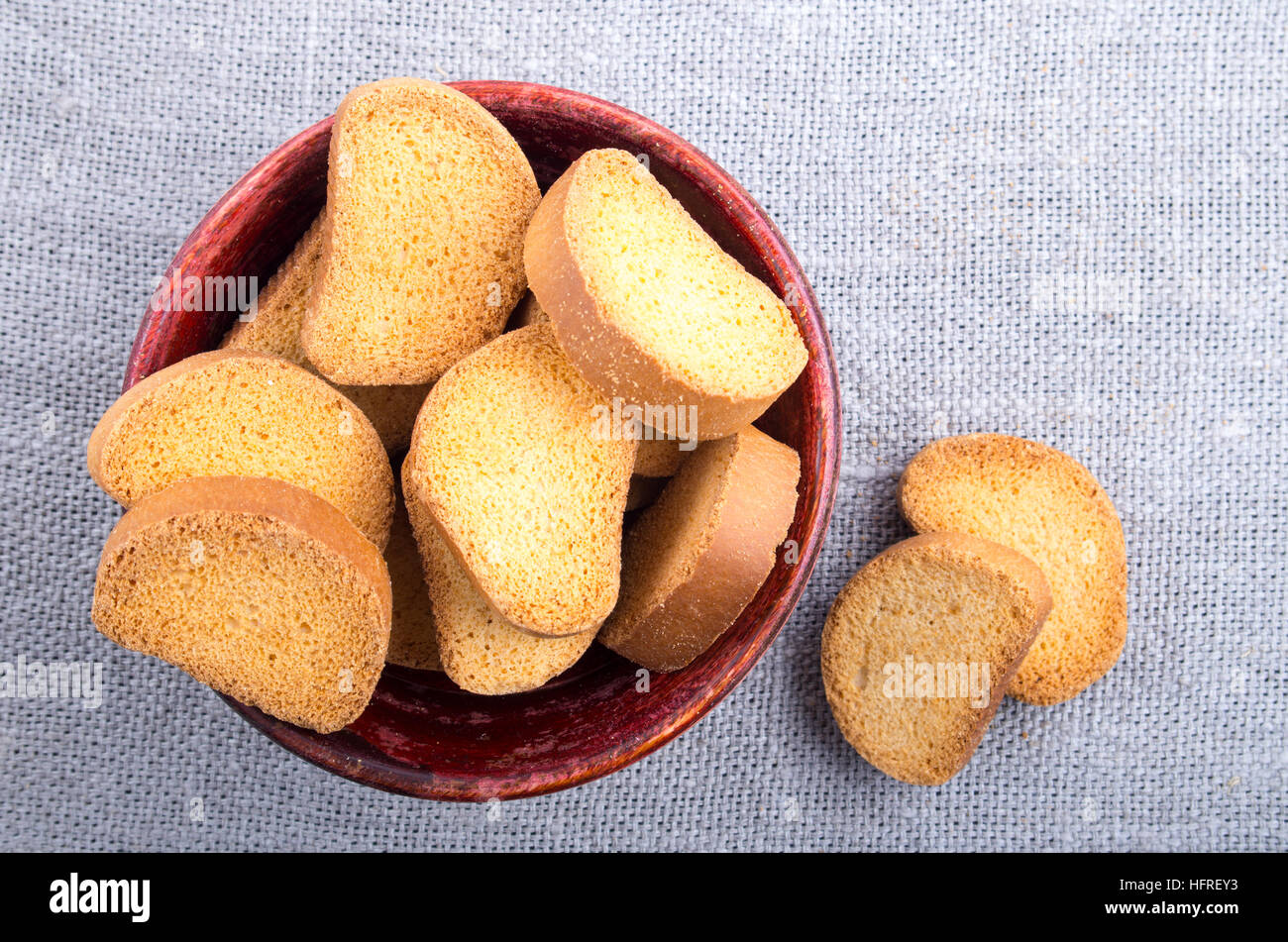 Fette di fette biscottate nella vecchia ciotola di legno su tela panno grigio. Vista dall'alto di close-up. Foto Stock