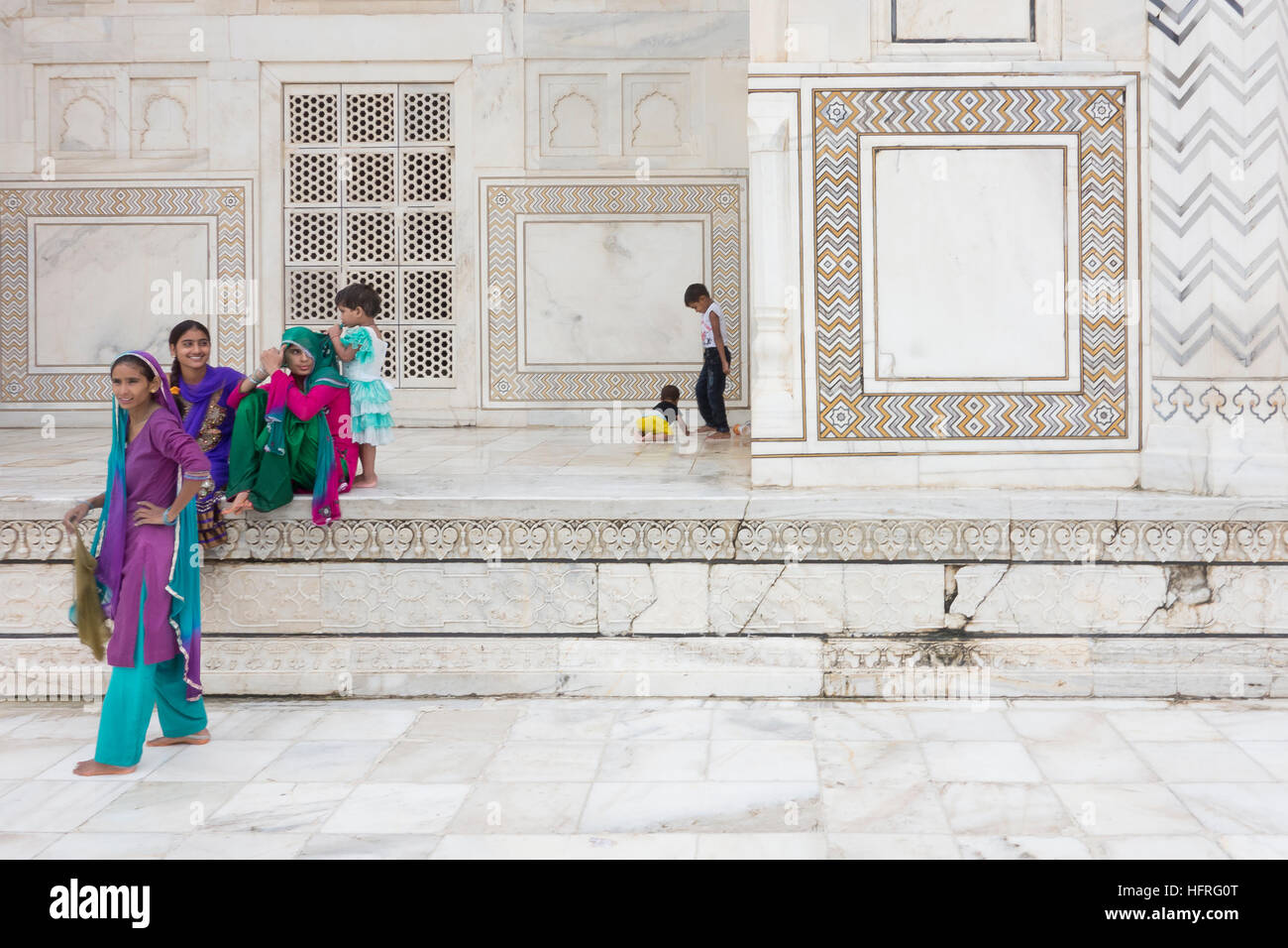 Donna sorridente e giocare con i bambini che indossano vestiti colorati rilassante sul marmo bianco sullo sfondo del Taj Mahal, India. Foto Stock