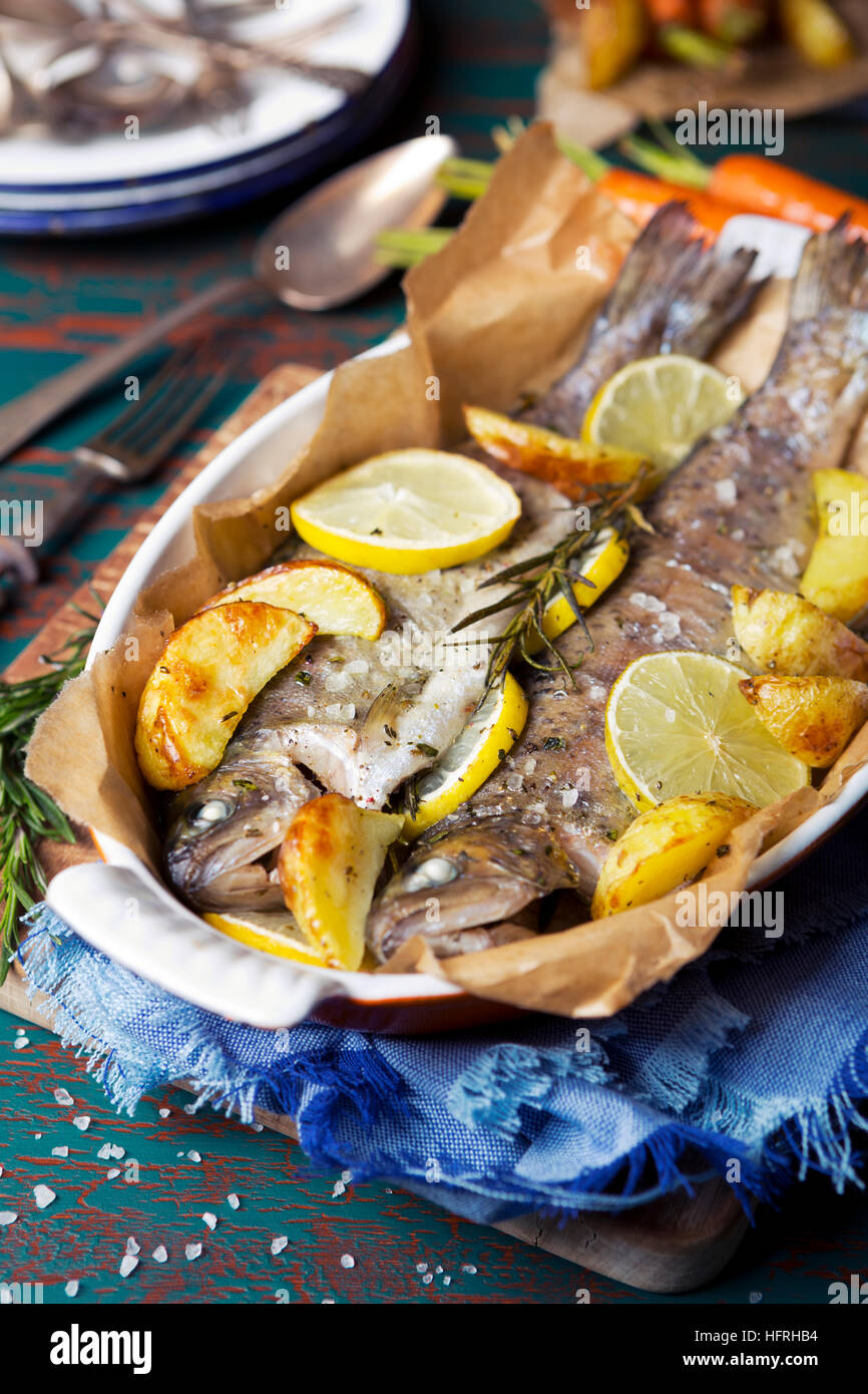 Un forno Arrosto di trota in una casseruola su un tavolo rustico. Con carote e patate sul lato. Foto Stock