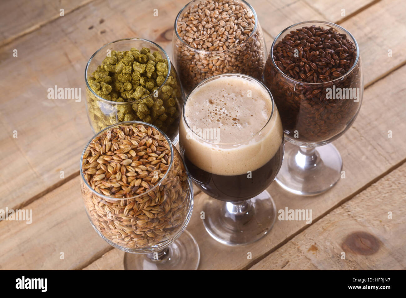 Bicchieri pieni di birra scura, differenti malto e luppolo su uno sfondo di legno Foto Stock