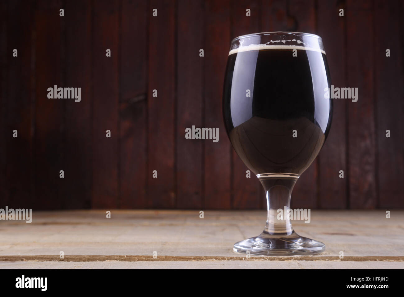 Bicchiere pieno di birra scura su uno sfondo di legno Foto Stock