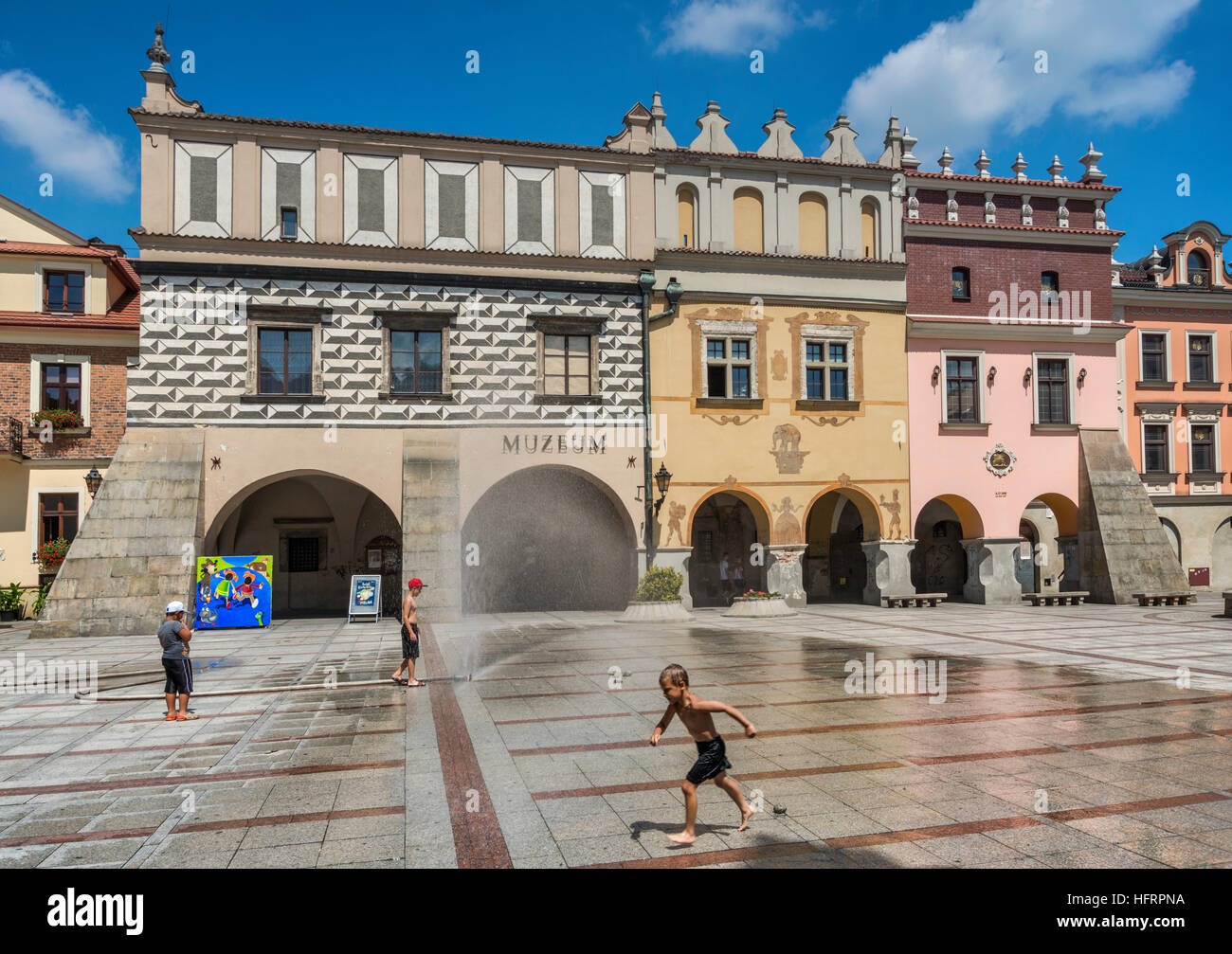Bambini che giocano al tubo flessibile di acqua in una calda giornata estiva, le case borghesi n. 19, 20, 21, la posizione del Museo Regionale, a Rynek di Tarnów, Malopolska, Polonia Foto Stock