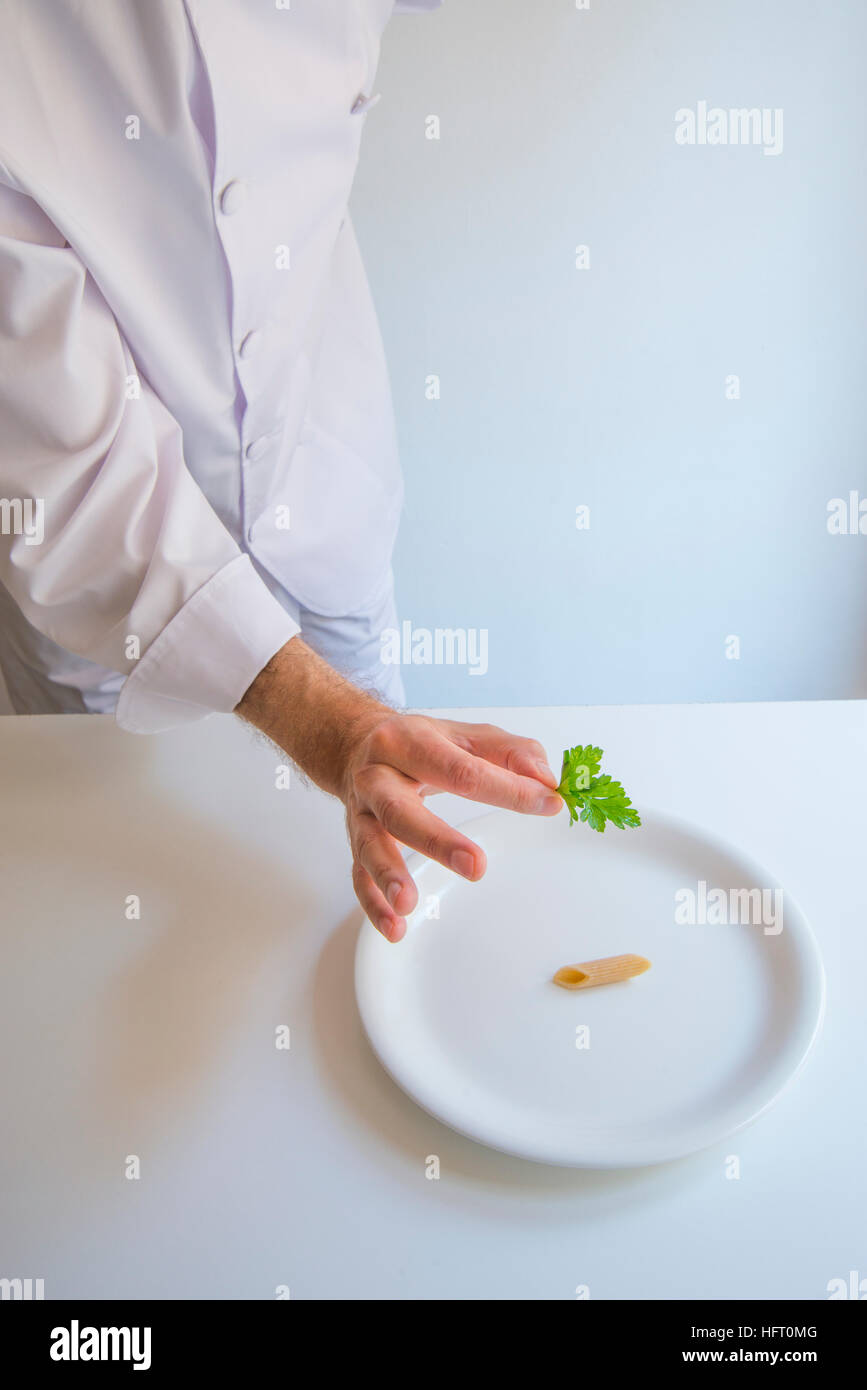 La nouvelle cuisine: minimalismo. Umoristico. Lo Chef mettendo una foglia di prezzemolo sulla parte superiore di un singolo maccheroni. Foto Stock