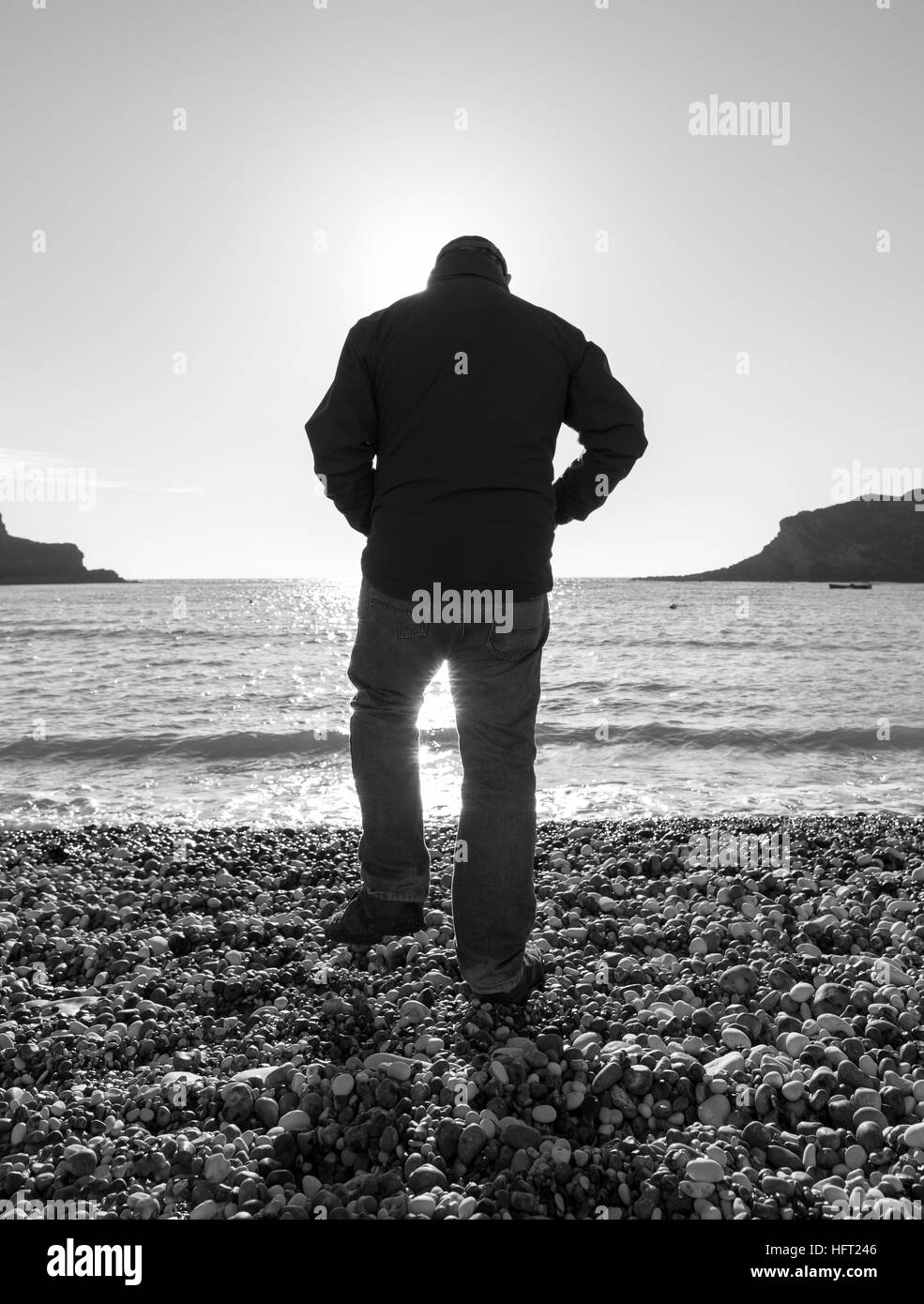 Uomo in abbigliamento invernale fredda giornata di sole sulla spiaggia ghiaiosa Foto Stock