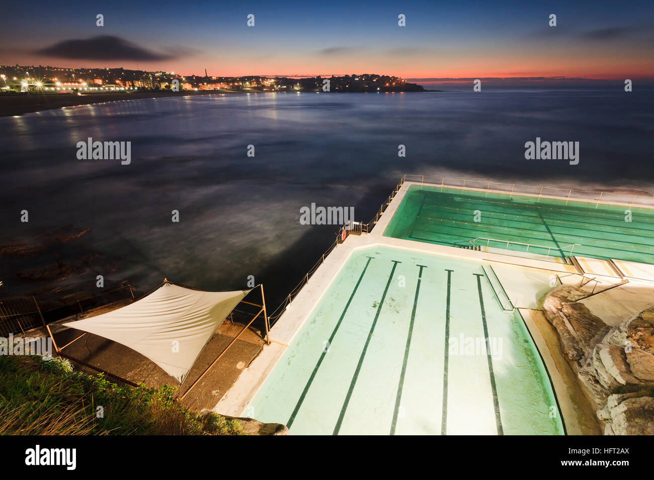 Sydney Bondi Beach a sunrise dal di sopra. Frammento di roccia publich piscina illuminata e sfocata ocean verso Rising Sun e dei sobborghi circostanti. Foto Stock