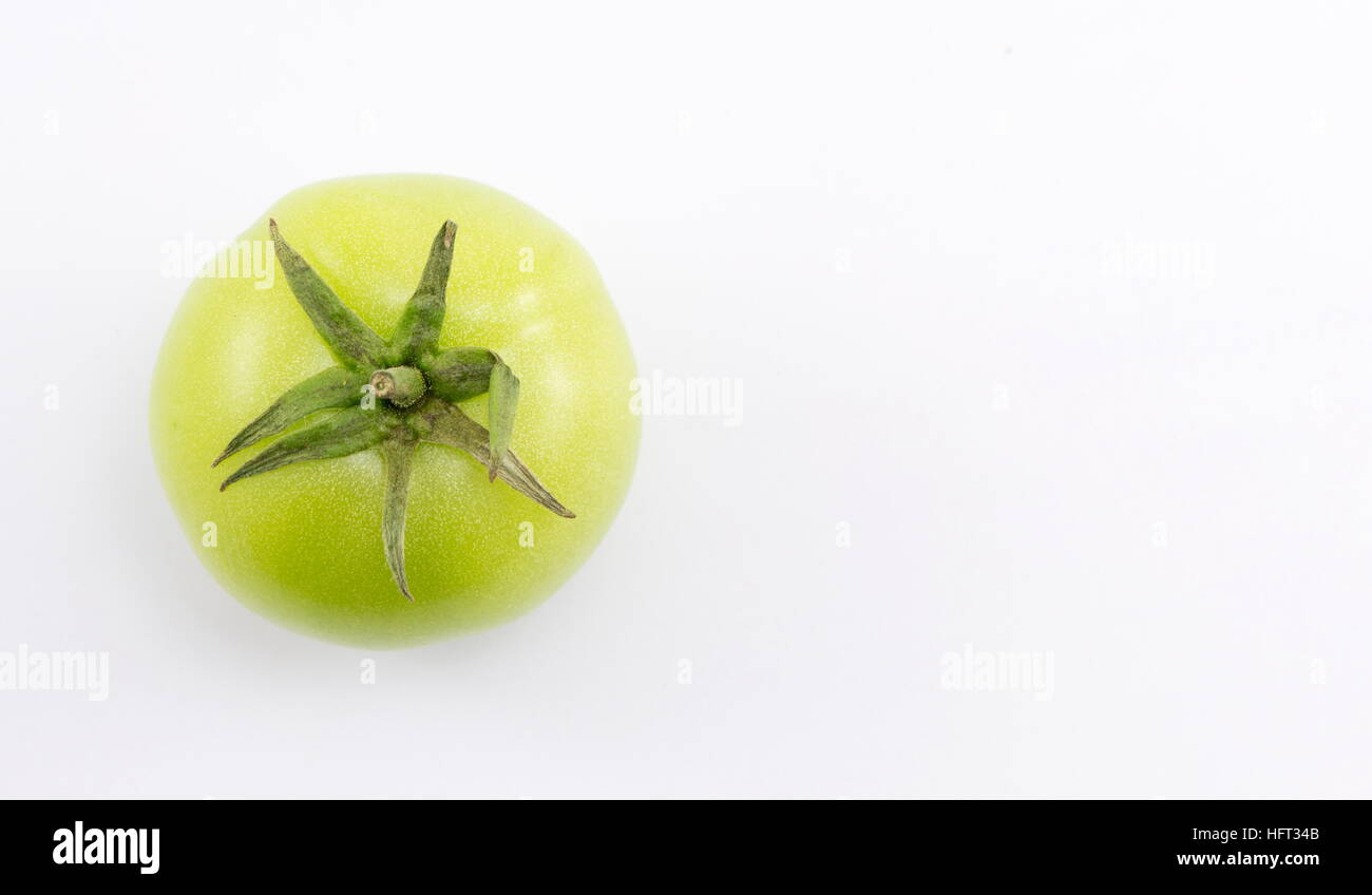 Single pomodoro verde su sfondo bianco Foto Stock