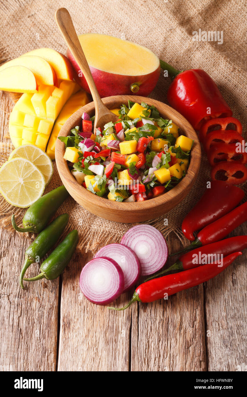 Salsa messicana con mango, il coriandolo, cipolle e peperoni vicino fino in una ciotola di legno e gli ingredienti sul piano verticale. Foto Stock